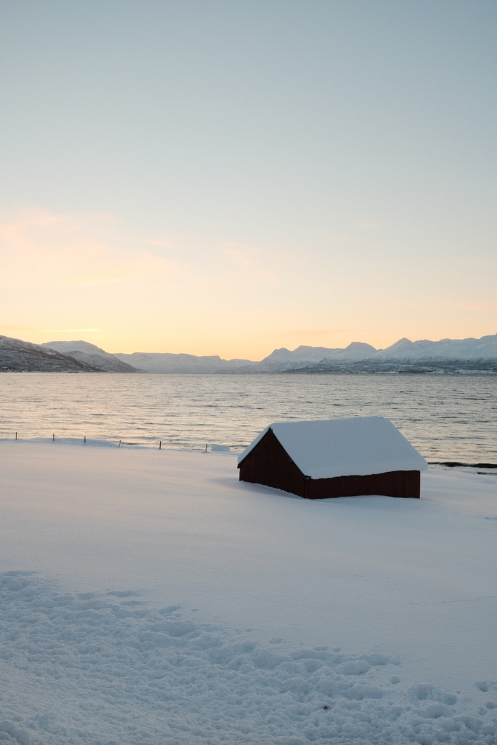 A red cabin beside a snow-covered shoreline